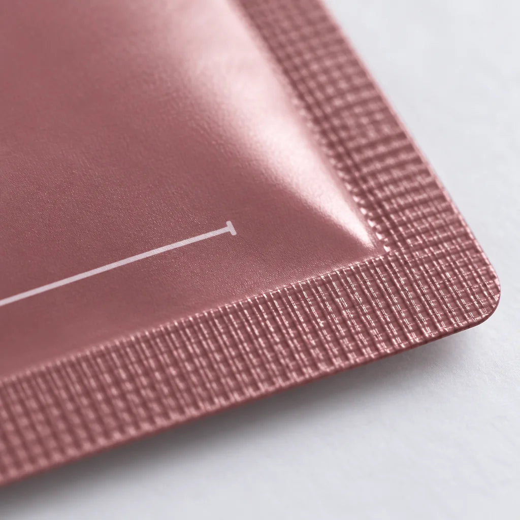 An extreme macro photograph of one corner of the exact foil collagen mask sachet from the reference.