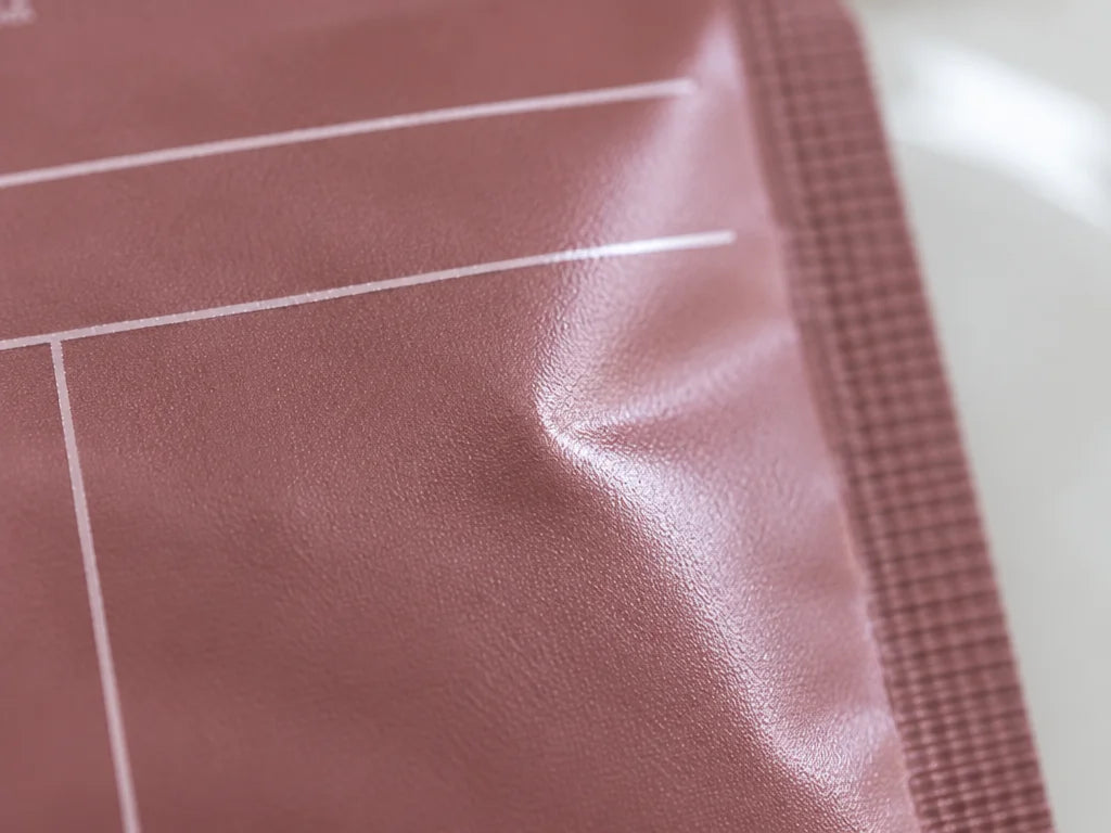 A macro photograph of the central foil surface of the exact collagen mask sachet from the reference,